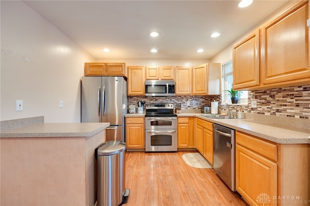 kitchen featuring light wood-style flooring, stainless steel appliances, a sink, light countertops, and decorative backsplash