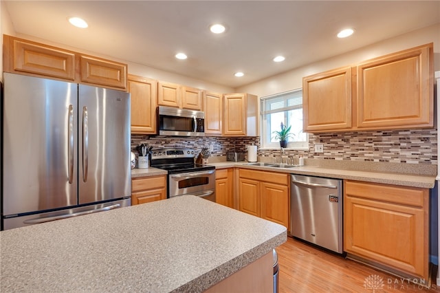 kitchen with light countertops, appliances with stainless steel finishes, light brown cabinets, a sink, and light wood-type flooring