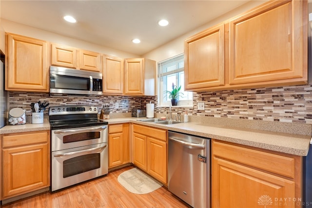 kitchen featuring stainless steel appliances, a sink, light countertops, light wood-type flooring, and decorative backsplash