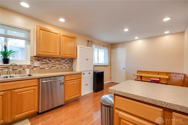 kitchen with tasteful backsplash, light countertops, a sink, light wood-type flooring, and dishwasher