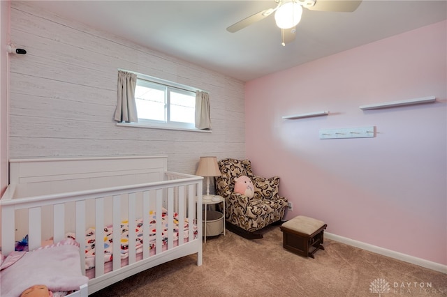 carpeted bedroom with a crib, a ceiling fan, and baseboards