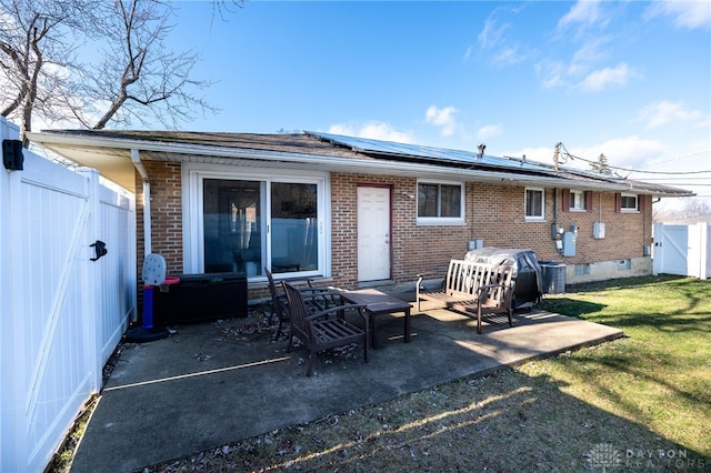 back of property with brick siding, a patio, a fenced backyard, and solar panels