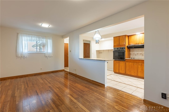 kitchen with kitchen peninsula, oven, light wood-type flooring, and decorative backsplash