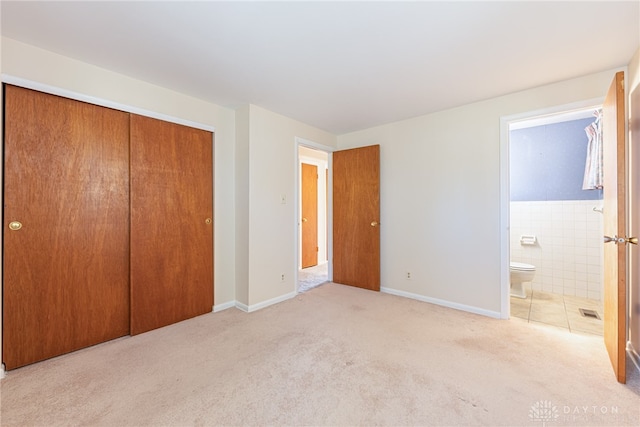 unfurnished bedroom featuring light carpet, a closet, tile walls, and ensuite bathroom