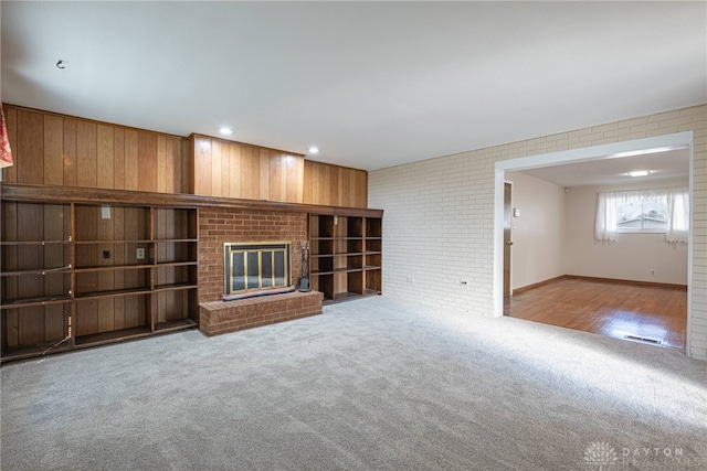 unfurnished living room featuring a fireplace, brick wall, and carpet