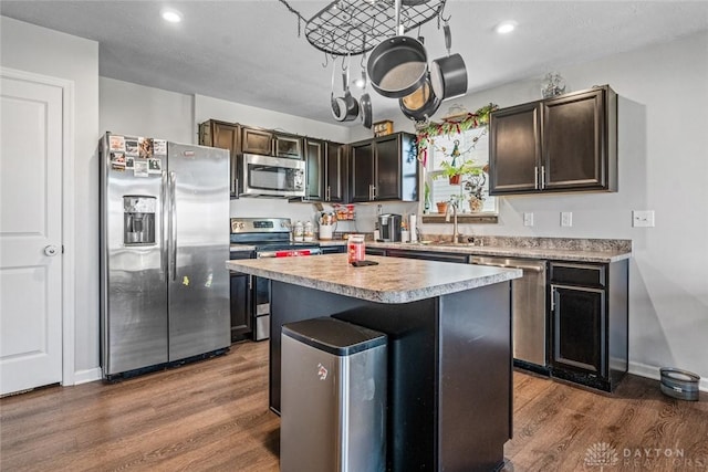 kitchen with a kitchen bar, appliances with stainless steel finishes, dark brown cabinetry, dark wood-type flooring, and a center island