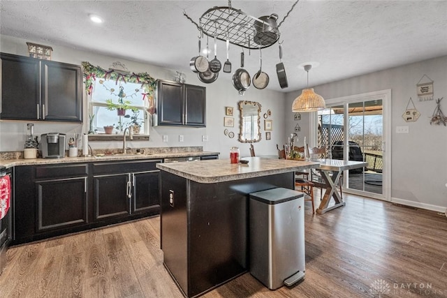 kitchen with a textured ceiling, sink, pendant lighting, a center island, and light hardwood / wood-style floors