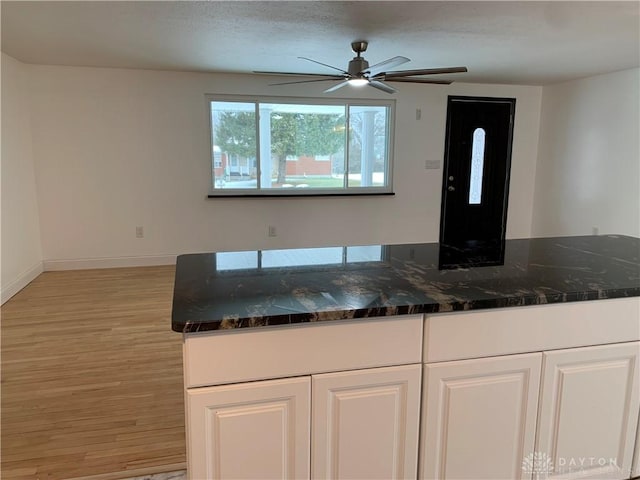 kitchen featuring white cabinets, light hardwood / wood-style floors, ceiling fan, and dark stone counters