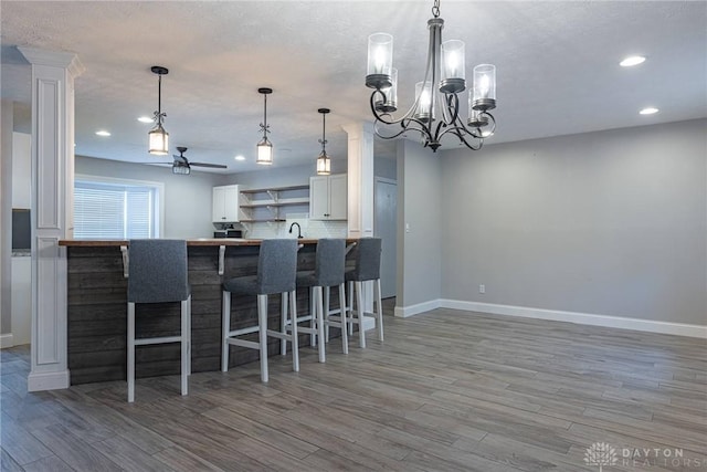 kitchen with kitchen peninsula, tasteful backsplash, a breakfast bar, hardwood / wood-style flooring, and white cabinets