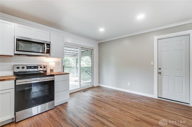 kitchen with ornamental molding, stainless steel appliances, light hardwood / wood-style flooring, white cabinets, and butcher block countertops