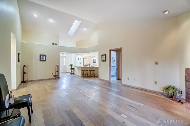 living room with a skylight, high vaulted ceiling, and light hardwood / wood-style floors