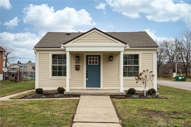 bungalow-style house with a porch, a shingled roof, and a front lawn