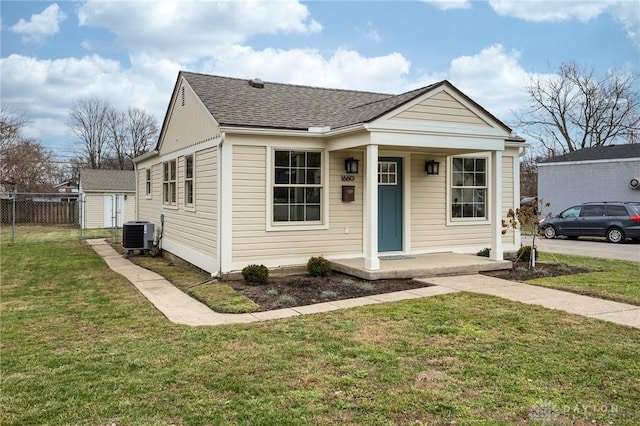 bungalow featuring a porch, fence, roof with shingles, a front yard, and central AC unit