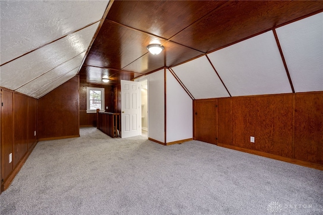 additional living space featuring light carpet, wooden walls, and vaulted ceiling