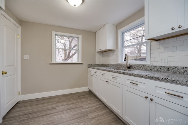 kitchen with light stone countertops, sink, tasteful backsplash, white cabinets, and light wood-type flooring