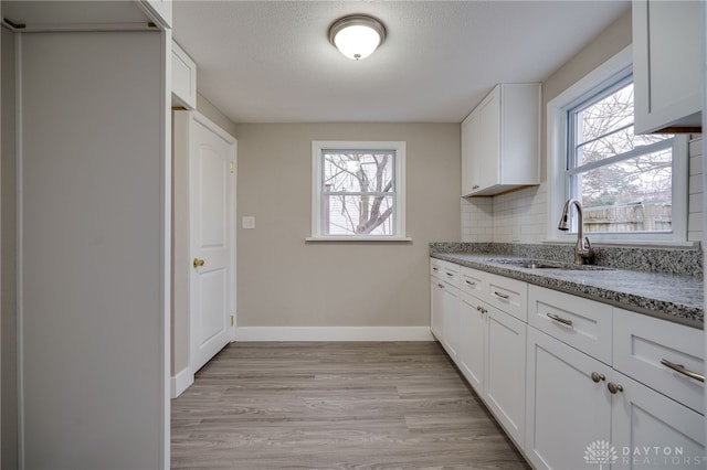 kitchen with stone counters, white cabinetry, sink, a healthy amount of sunlight, and decorative backsplash