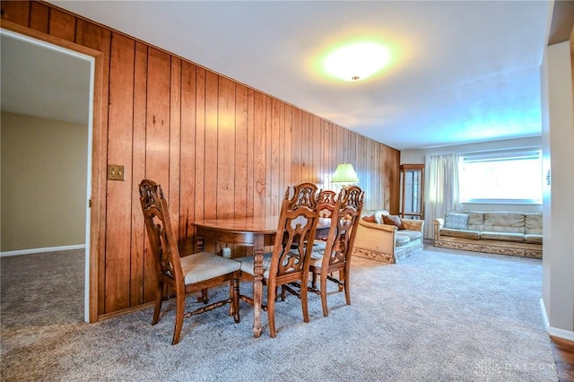 carpeted dining space featuring wood walls