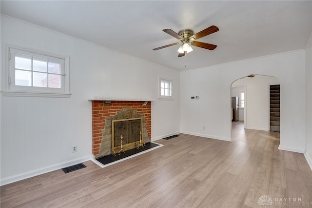 unfurnished living room featuring a brick fireplace, ceiling fan, ornamental molding, and light wood-type flooring