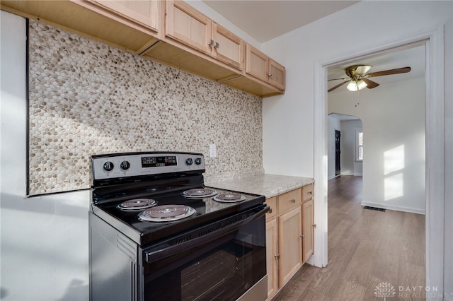 kitchen with ceiling fan, backsplash, stainless steel electric stove, light brown cabinetry, and light wood-type flooring