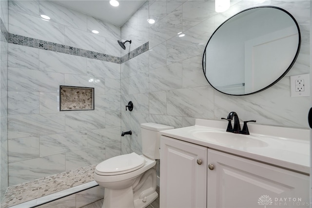 bathroom with vanity, toilet, tiled shower, and tile walls