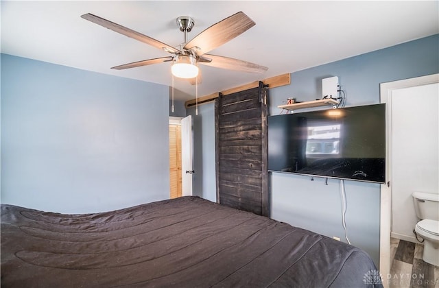 unfurnished bedroom with a barn door, ceiling fan, and wood-type flooring