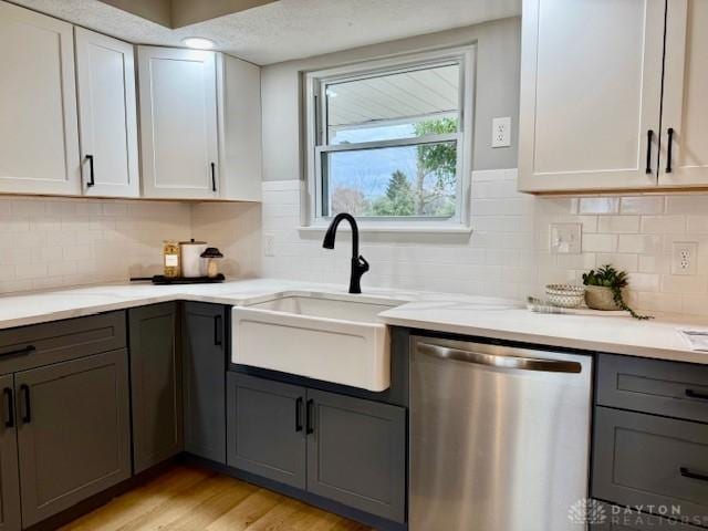 kitchen with decorative backsplash, light wood-type flooring, white cabinets, sink, and dishwasher