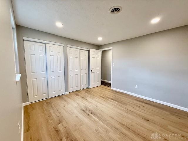 unfurnished bedroom with light hardwood / wood-style floors and two closets