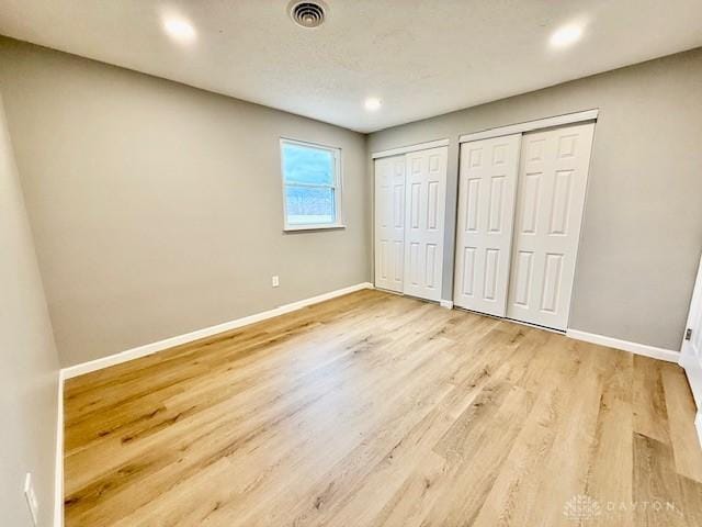 unfurnished bedroom with two closets and light hardwood / wood-style flooring