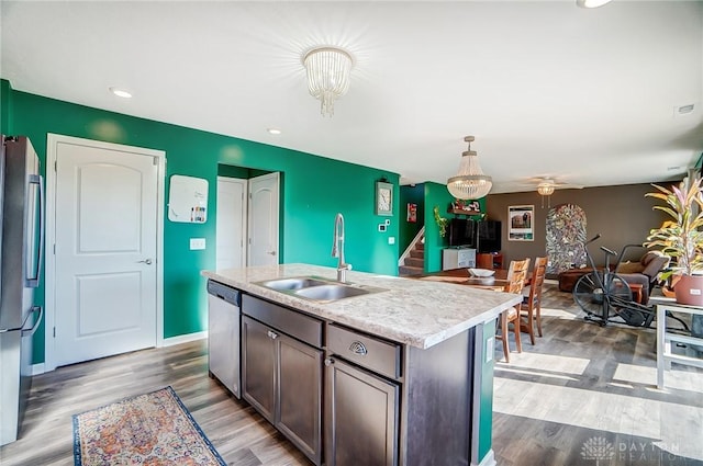 kitchen with appliances with stainless steel finishes, dark brown cabinetry, a kitchen island with sink, sink, and hanging light fixtures