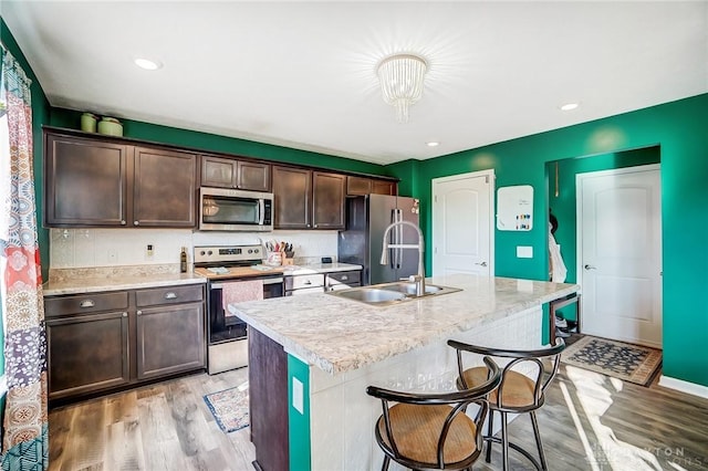 kitchen featuring a center island with sink, sink, light wood-type flooring, dark brown cabinets, and stainless steel appliances