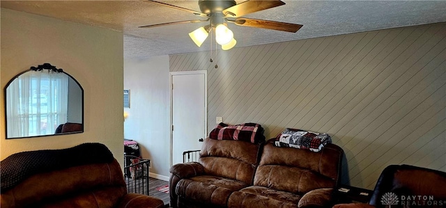 living room with ceiling fan, wood walls, and a textured ceiling