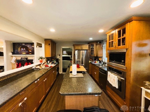 kitchen with sink, a center island, dark hardwood / wood-style flooring, dark stone counters, and appliances with stainless steel finishes