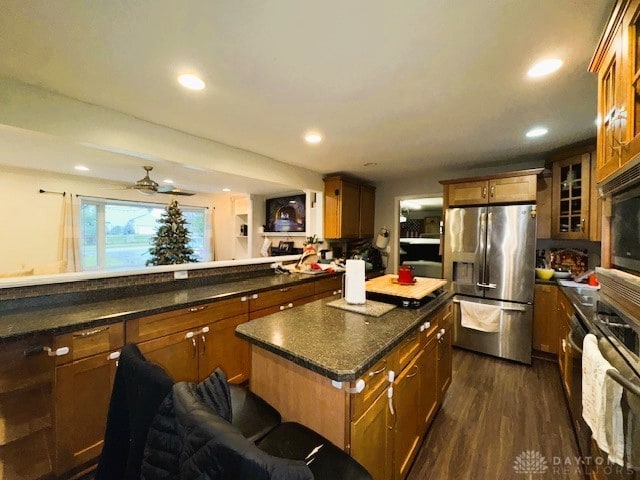 kitchen with ceiling fan, dark hardwood / wood-style flooring, stainless steel refrigerator with ice dispenser, a kitchen bar, and a kitchen island