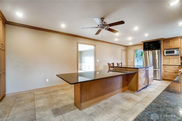 kitchen featuring ceiling fan, stainless steel fridge, dark stone countertops, ornamental molding, and a kitchen island