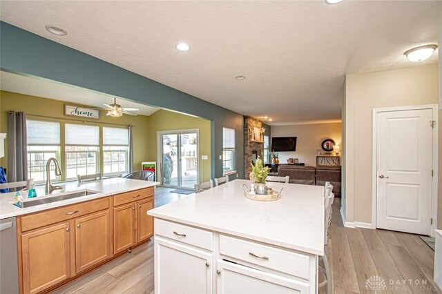 kitchen featuring dishwasher, a center island, sink, ceiling fan, and light wood-type flooring