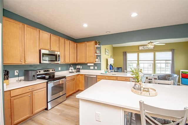 kitchen featuring a kitchen breakfast bar, sink, light hardwood / wood-style flooring, ceiling fan, and stainless steel appliances