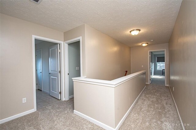 hall with light colored carpet and a textured ceiling