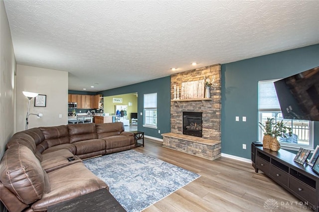 living room featuring a stone fireplace, a textured ceiling, and light wood-type flooring