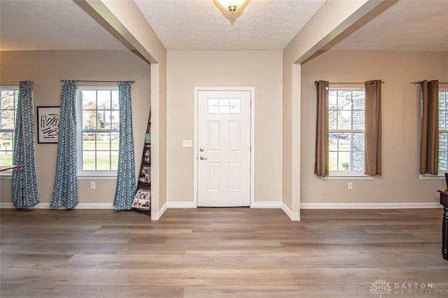 foyer featuring a textured ceiling, baseboards, and wood finished floors