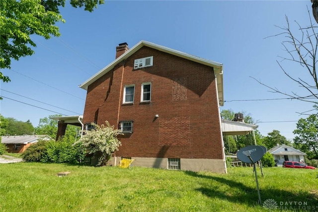 view of side of property featuring a chimney, a lawn, and brick siding