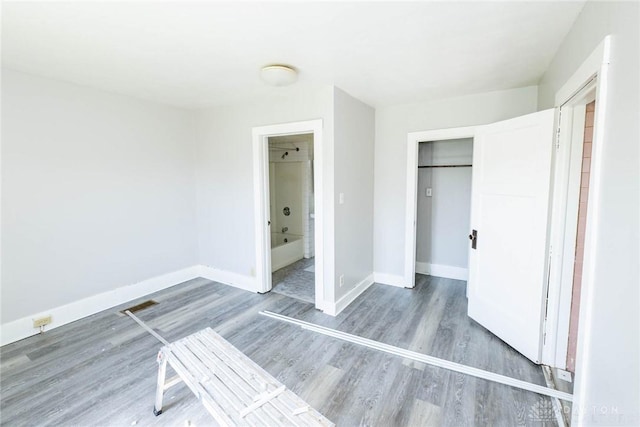 unfurnished bedroom featuring wood-type flooring, connected bathroom, and a closet