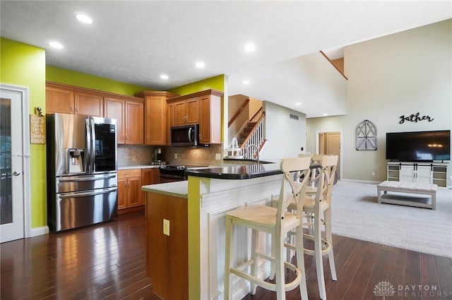 kitchen featuring dark hardwood / wood-style floors, appliances with stainless steel finishes, tasteful backsplash, a kitchen bar, and kitchen peninsula