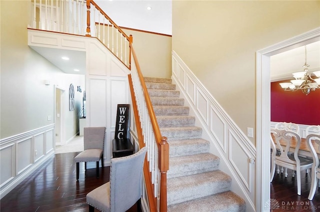 stairs featuring a towering ceiling, an inviting chandelier, a decorative wall, and wood finished floors