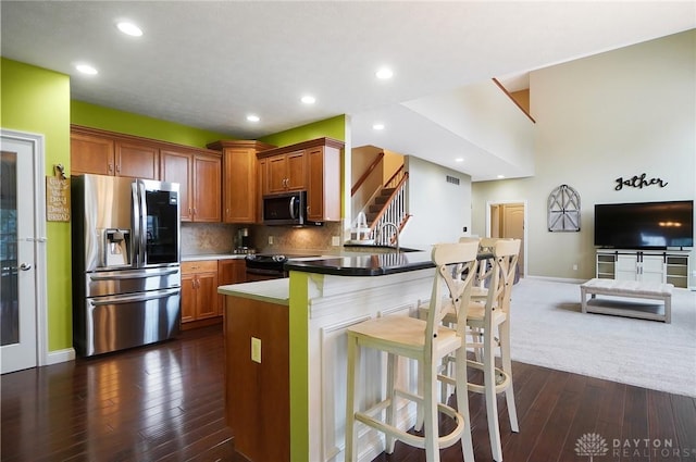 kitchen with open floor plan, appliances with stainless steel finishes, brown cabinets, decorative backsplash, and a kitchen bar