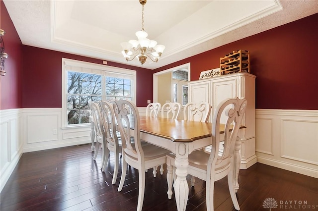 dining area with a chandelier, wainscoting, a raised ceiling, and dark wood-style floors