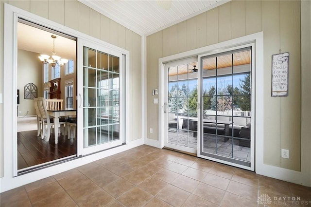 doorway with wood walls, tile patterned flooring, a chandelier, and baseboards