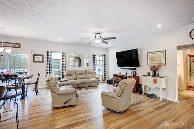 living room featuring ceiling fan with notable chandelier, a healthy amount of sunlight, and light wood-type flooring