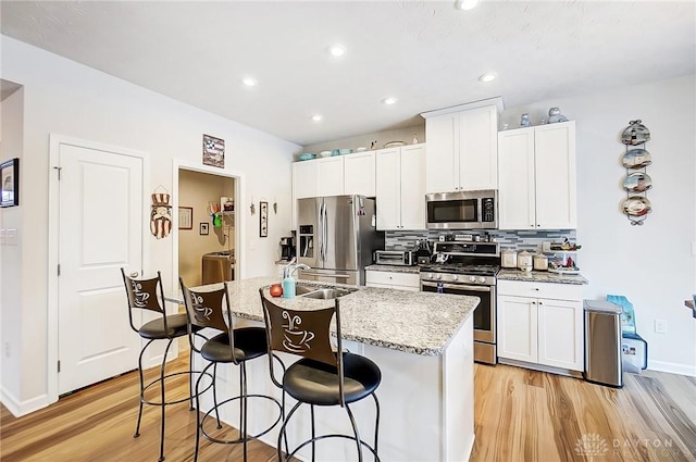 kitchen with a center island with sink, sink, light hardwood / wood-style flooring, light stone counters, and stainless steel appliances