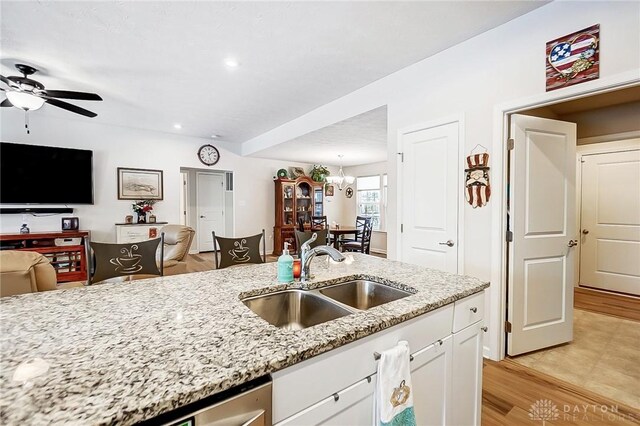 kitchen featuring light stone counters, ceiling fan with notable chandelier, sink, light hardwood / wood-style flooring, and white cabinets