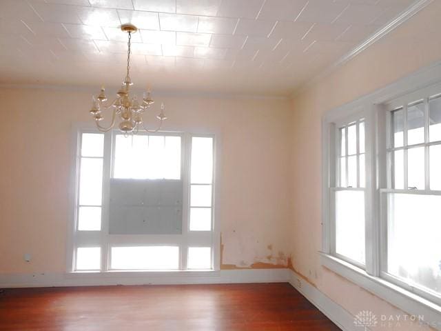 empty room featuring plenty of natural light, hardwood / wood-style floors, ornamental molding, and a chandelier